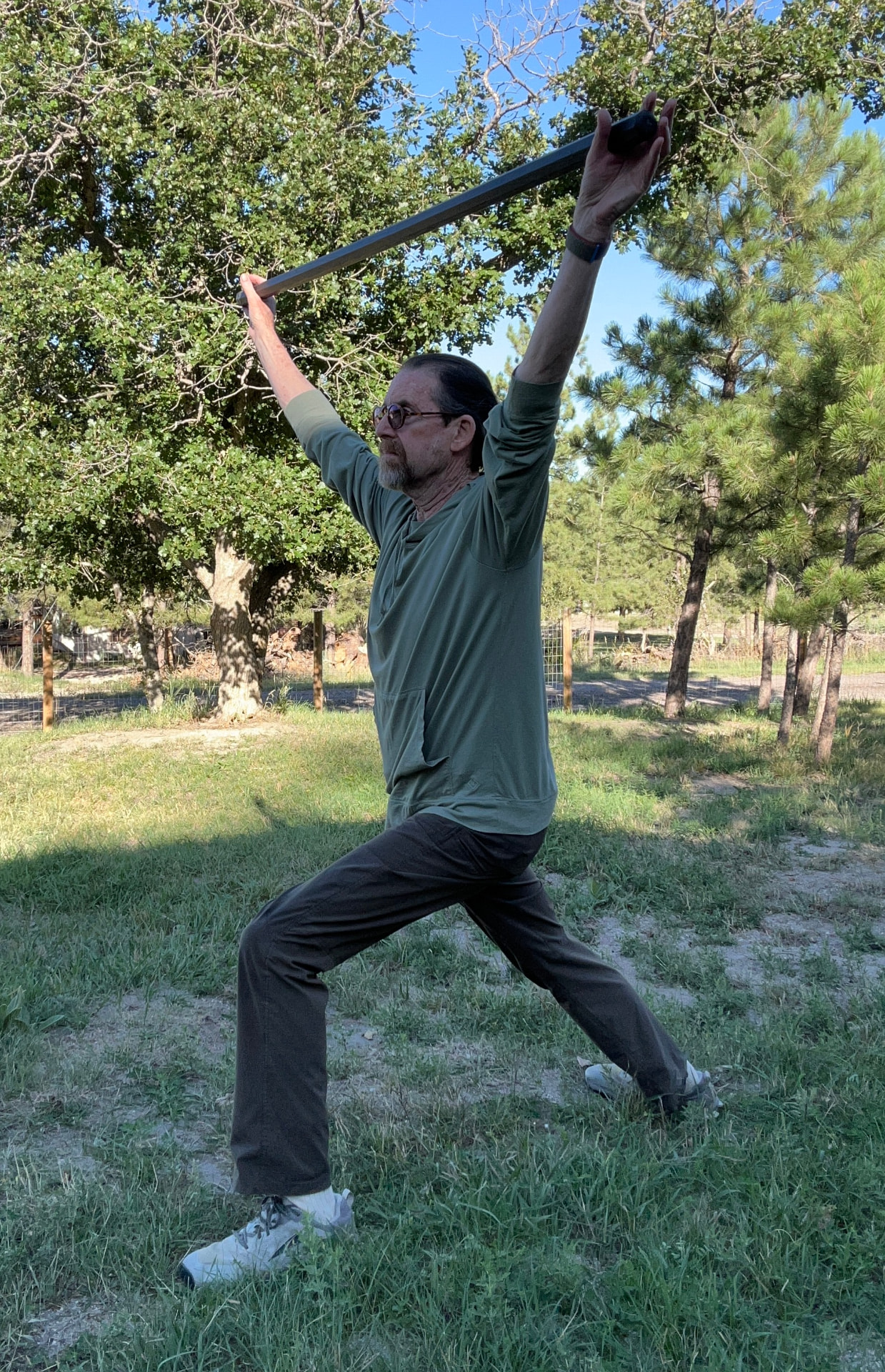 Marc Tull stretching in a wide stance with a staff raised overhead